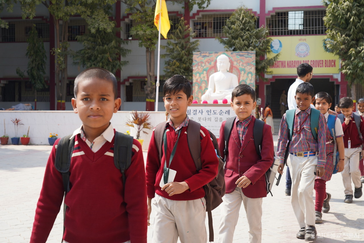 카이야 DAV학교에서 하교하는 아이들의 뒤로 순례단을 이끄는 부처님이 미소짓고 있다.