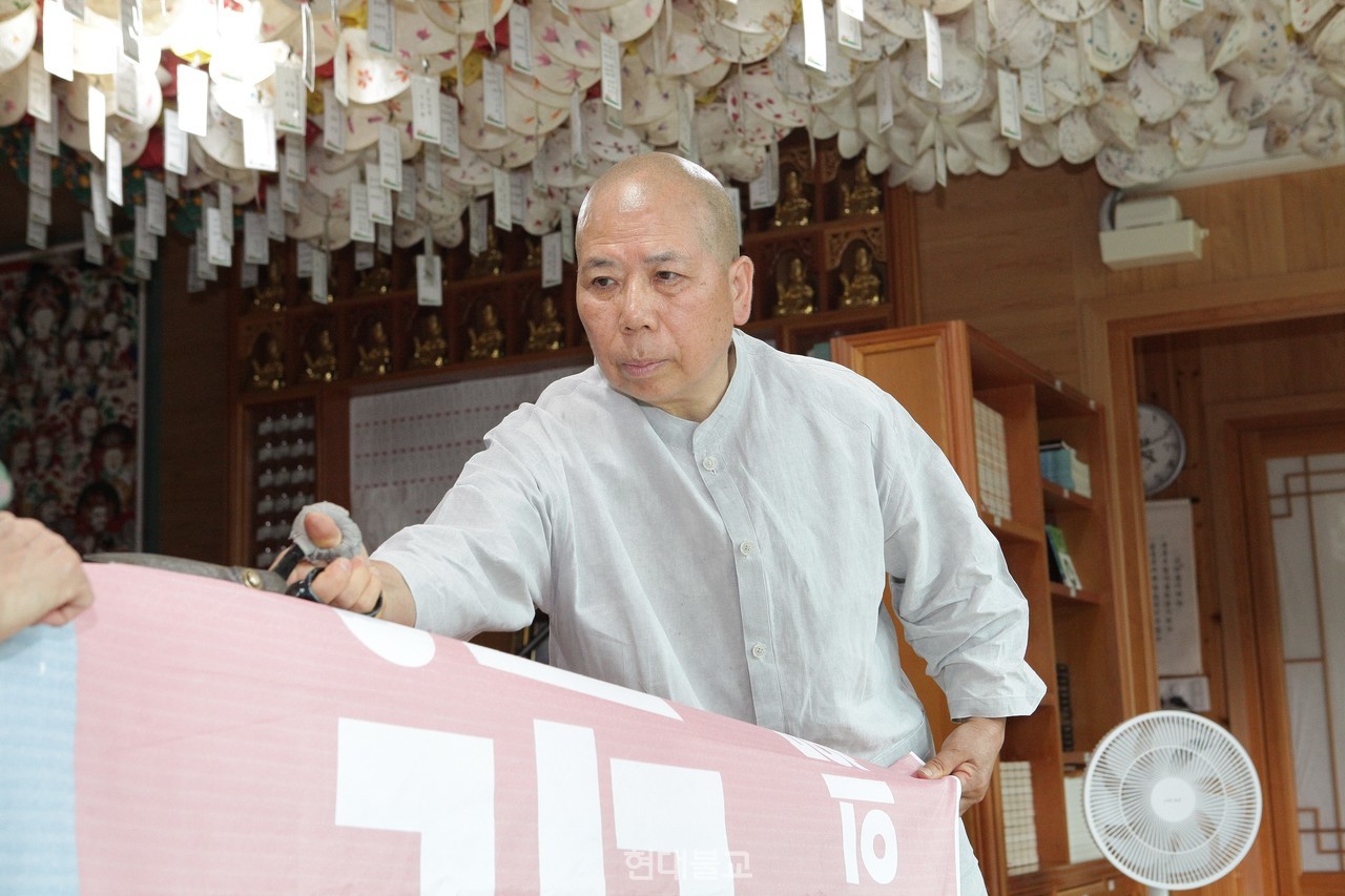 정찬 스님이 가방 바느질에 앞서 폐현수막을 자르고 있다.
