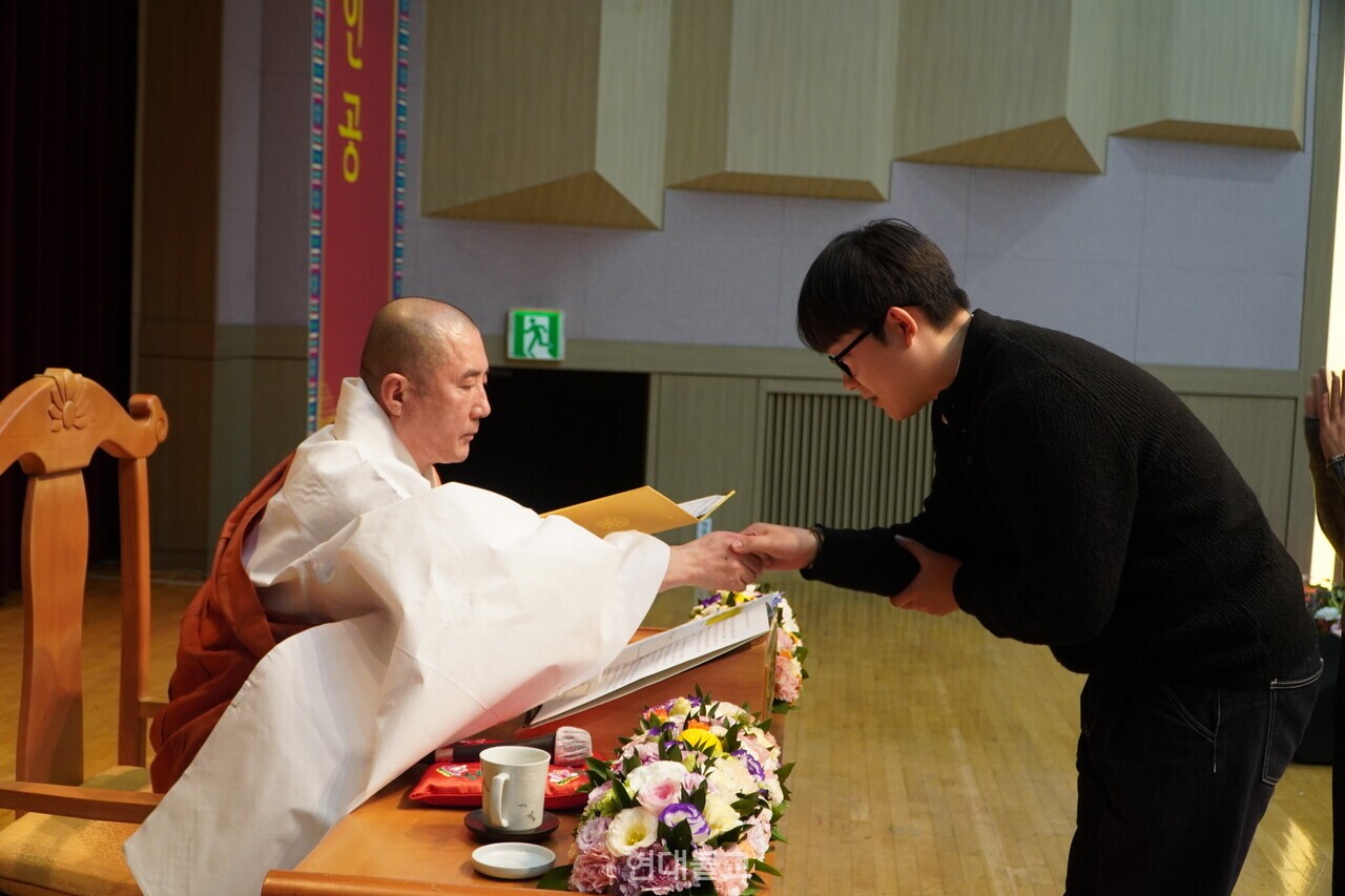 돈관 스님이 학생 대표 정재훈 학생에게 계첩을 전달하고 있다. 