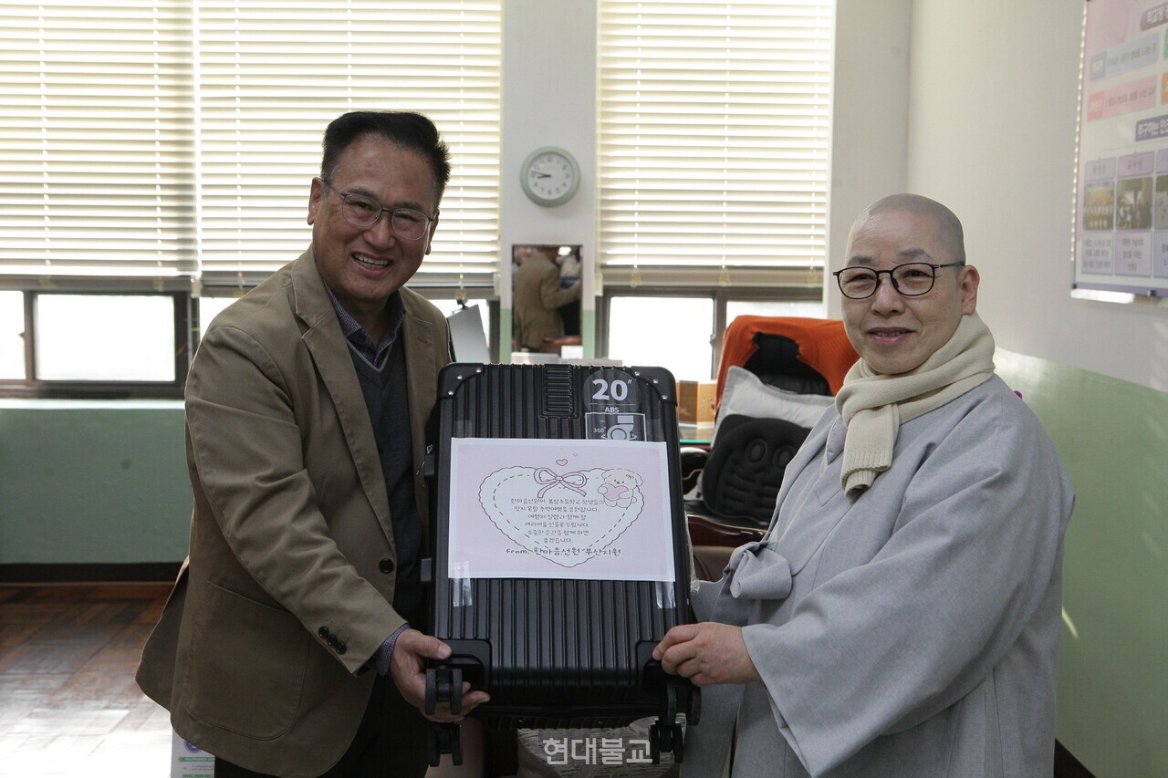 학생들에게 전달될 새 캐리어를 함께 들어 보이는 박용호 교장과 혜도 스님.