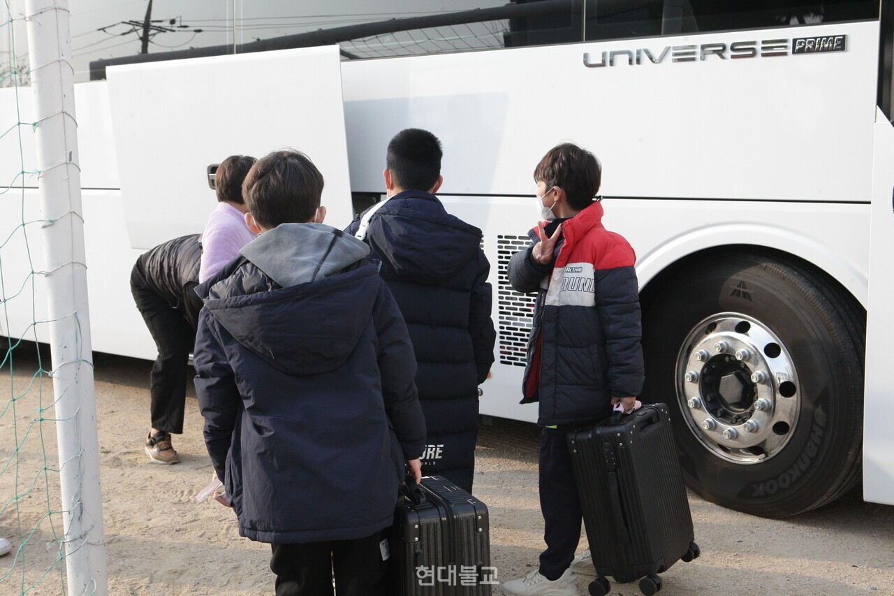 버스 짐칸 앞에서 캐리어를 차례로 싣는 학생들.